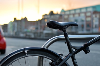 Close up photo of bike seat and wheel, with city buildings in the background