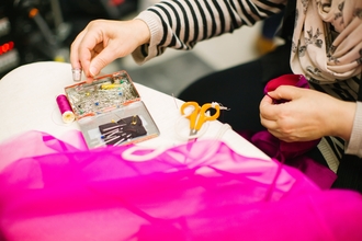 A person with scissors and sewing kit and pink fabric