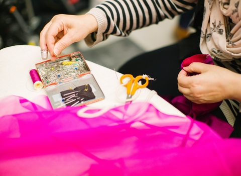 A person with scissors and sewing kit and pink fabric